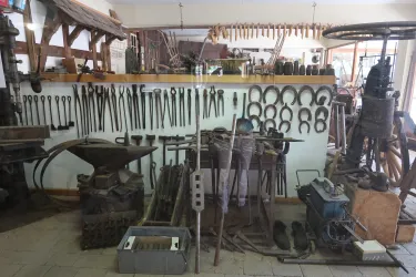 Eine handwerkliche Werkstatt mit zahlreichen Werkzeugen an der Wand. Auf dem Boden sind verschiedene Geräte und Materialien zum Arbeiten zu sehen.