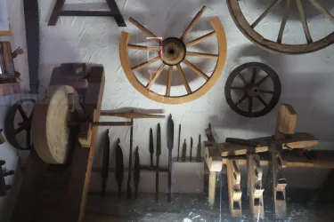 Eine Sammlung von Holzrädern und Werkzeugen ist an der Wand befestigt. Die Materialien zeigen handwerkliches Geschick und traditionelle Fertigungstechniken.