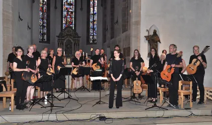 Eine Gruppe von Musikern steht in einer Kirche und spielt verschiedene Instrumente. Sie tragen schwarze Kleidung und sind auf ein Konzert vorbereitet.