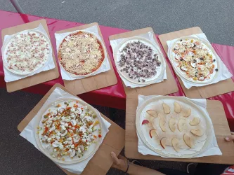 Sechs verschiedene Pizzen auf Holzplatten, jede mit einer einzigartigen Belaggestaltung. Die Pizzen zeigen bunte Zutaten wie Gemüse, Obst und Käse.