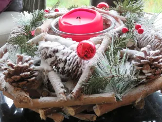 Ein festlicher Adventskranz mit einer roten Kerze, Tannenzweigen und dekorativen roten Kugeln. Der Kranz ist mit einer leichten Schneeschicht bedeckt.