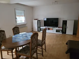 Ein gemütliches Wohnzimmer mit einem Essplatz und einem großen Fernseher. Der Raum hat helle Wände und einen Holzboden.