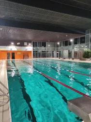 Ein gut beleuchtetes Schwimmbad mit klarem Wasser und roten Bahnmarkierungen. Die Umgebung ist modern mit großen Fenstern und Glaswänden.