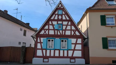 Ein charmantes Fachwerkhaus mit blauen Fensterläden. Der Himmel ist klar und es ist ein schöner Tag.