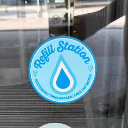 Ein Aufkleber mit der Aufschrift "Refill Station" zeigt einen Wassertropfen. Er informiert über kostenloses Trinkwasser am Standort.