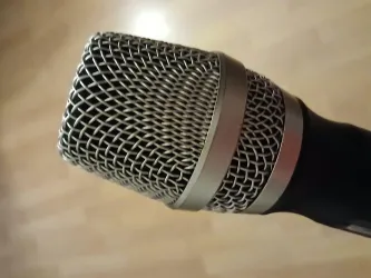 Ein Mikrofon mit einem metallischen Gitter und einem schwarzen Griff. Es ist gut beleuchtet und hat einen klaren Fokus.