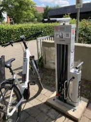 Eine Fahrradreparaturstation steht neben einem E-Bike. Die Station ist mit verschiedenen Werkzeugen und einer Luftpumpe ausgestattet.