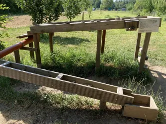 Eine Holzstruktur mit mehreren Rinnen steht im Grünen. Die Anlage scheint für ein Spiel oder eine Demonstration im Freien gedacht zu sein.