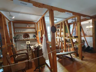 Ein historischer Friseursalon mit Holzwänden und alten Möbeln. Regale mit verschiedenen Gegenständen und Frisurausstattung sind sichtbar.