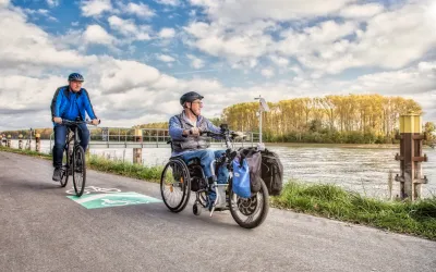 Zwei Radfahrer, einer davon im Rollstuhl, radeln entlang des Rheins