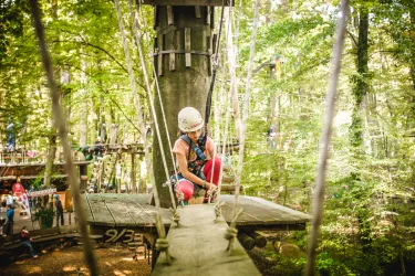 Mädchen kniet gesichert auf einer Plattform im Abenteuerpark Kandel