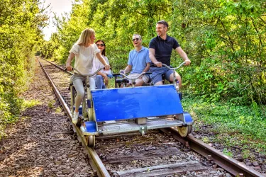 Zwei gut gelaunte Paare radeln mit einer Draisine durch ein Waldstück