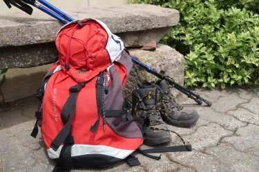roter Wanderrucksack mit Wanderschuhe und Stöcken