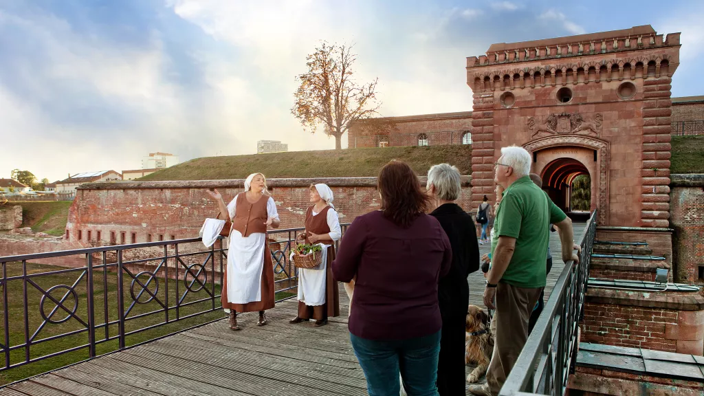 Eine Gruppe lauscht gespannt den Worten von zwei Bauersfrauen vor dem Weißenburger Tor