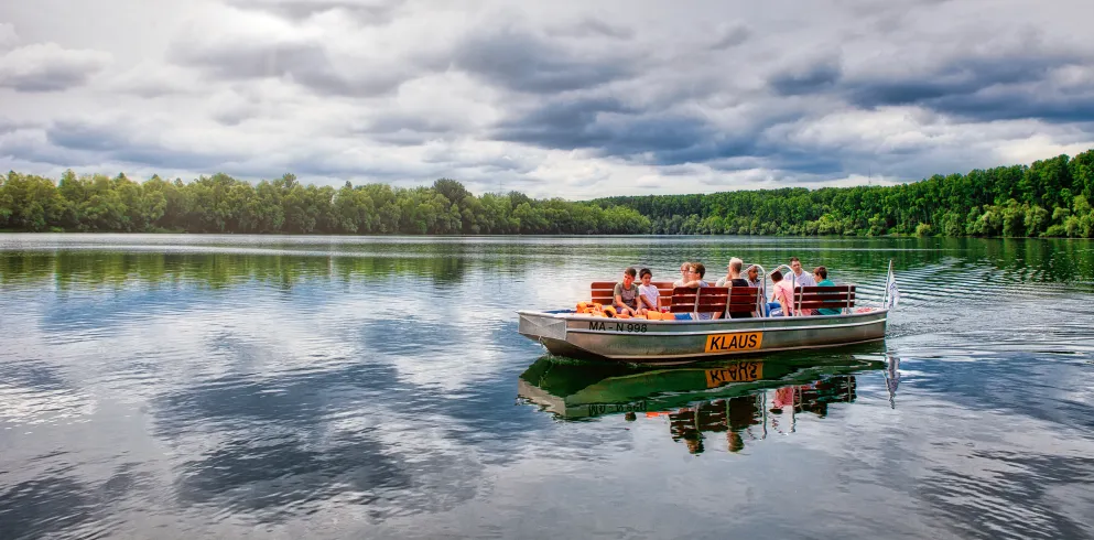 Eine Gruppe fährt auf einem Nachen über das stille Wasser des Althreins