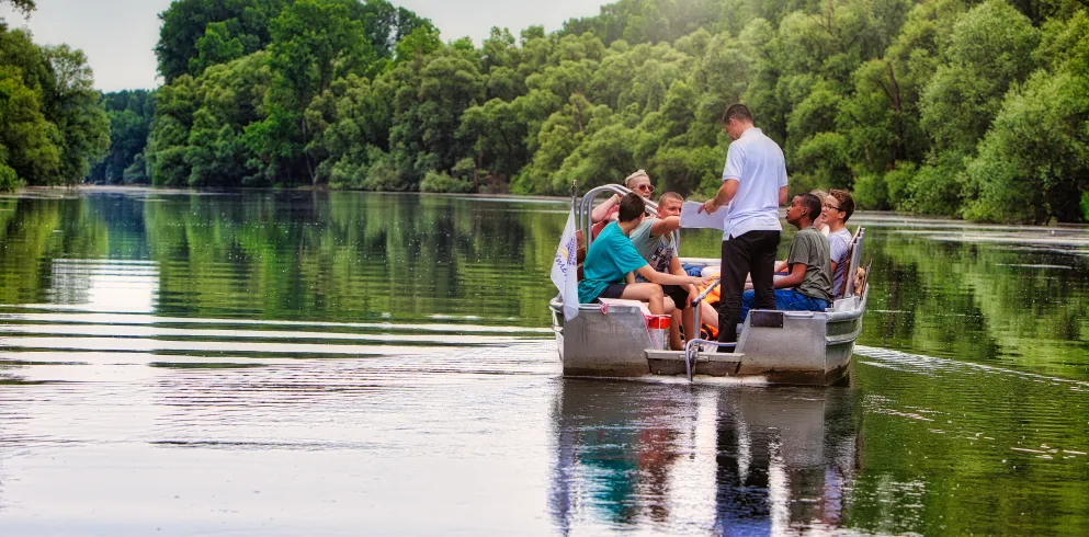 Eine Gruppe Jugendlicher bekommt in einem Nachen sitzend Erklärungen zur Natur durch den Bootsführer