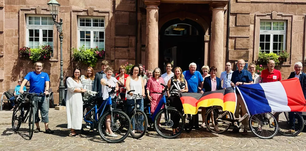 Eine Gruppe aus Touristikern steht mit Fahrrädern und einer deutschen sowie französischen Flagge vor dem imposanten Rathaus in Ettlingen