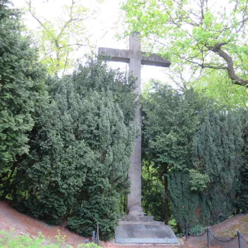 Ein großes Kreuz steht umgeben von dichten grünen Bäumen. Der Ort vermittelt eine ruhige und besinnliche Atmosphäre.