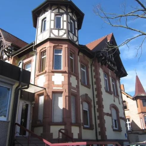 Ein historisches Gebäude mit einem Turm und einem schönen, gemischten Fachwerkstil. Der Himmel ist klar und blau.
