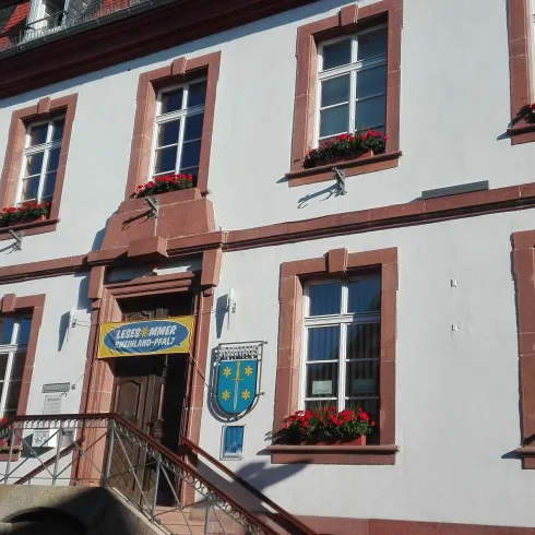 Ein schönes Gebäude mit weißen Wänden und roten Fensterrahmen. Blumenkästen unter den Fenstern sorgen für Farbtupfer.