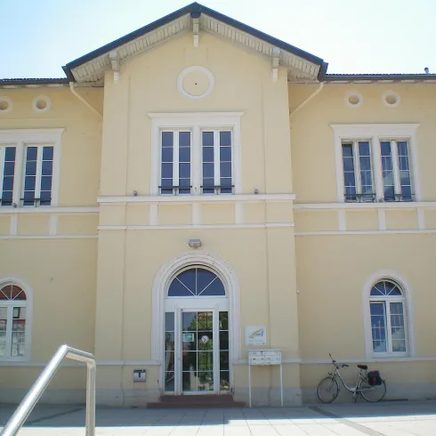 Ein hellgelbes Gebäude mit mehreren Fenstern und einem großen Eingang. Neben dem Eingang steht ein Fahrrad.