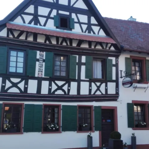 Ein traditionelles Fachwerkhaus mit grün gestrichenen Fensterläden. Die Fassade ist weiß mit schwarzem Holzrahmen.