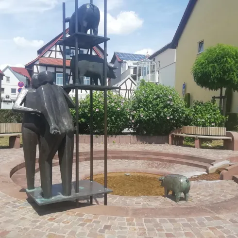 Eine moderne Skulptur aus Metall zeigt eine tierische Komposition in einem kleinen Park. Rund um die Skulptur sind Bänke und üppiges Grün.