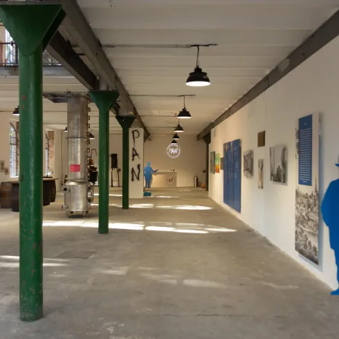 Ein weitläufiger Raum mit hohen Decken und grünen Säulen. An den Wänden befinden sich verschiedene Kunstwerke und Silhouetten.