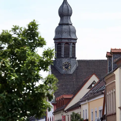 Ein schöner Ausblick auf eine Kirche mit einem markanten Turm. Im Vordergrund sind Bäume und eine malerische Straße zu sehen.