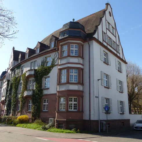 Ein historisches Gebäude mit einem charmanten Dach und Fenstern. Es ist von Bäume und Grünflächen umgeben.