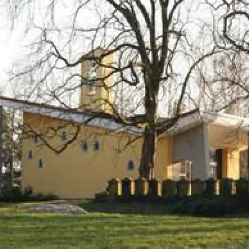 Ein kleines, gelbes Gebäude steht inmitten von Bäumen. Es hat einen modernen Stil und ist von einem gepflegten Garten umgeben.