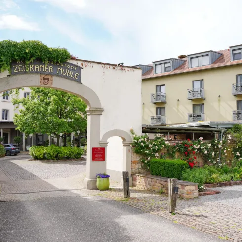 Ein einladender Eingang zu einem Hotel mit grünem dekorativem Efeu. In der Umgebung gibt es wunderschöne Blumen und eine gepflegte Landschaft.