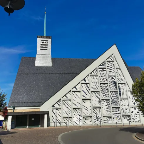 Eine moderne Kirche mit einem auffälligen Dach und einem schlichten, weißen Design. Der klare blaue Himmel verleiht dem Gebäude einen beeindruckenden Kontrast.