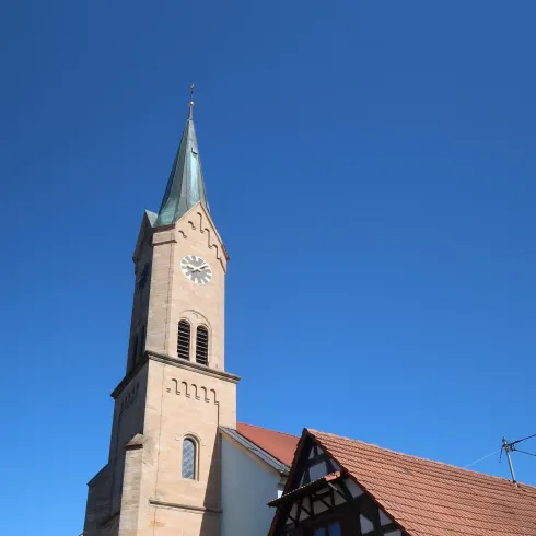 Ein malerisches Dorf mit einer hohen Kirche und einem traditionellen Fachwerkhaus. Der Himmel ist klar und blau.