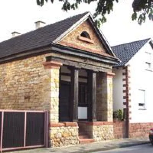 Ein charmantes, historisches Haus mit einem Steinfassade und dekorativen Details. Es steht an einer Straße, umgeben von anderen Häusern.