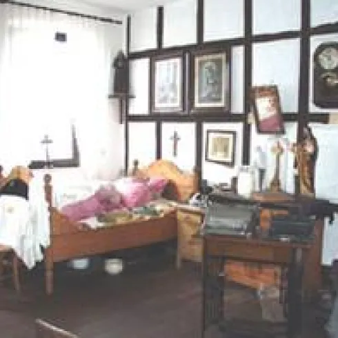 Ein gemütliches Schlafzimmer mit einem Holzbett und aufgeräumten Kissen. An den Wänden hängen Bilder und Uhren, und es gibt Möbel im traditionellen Stil.