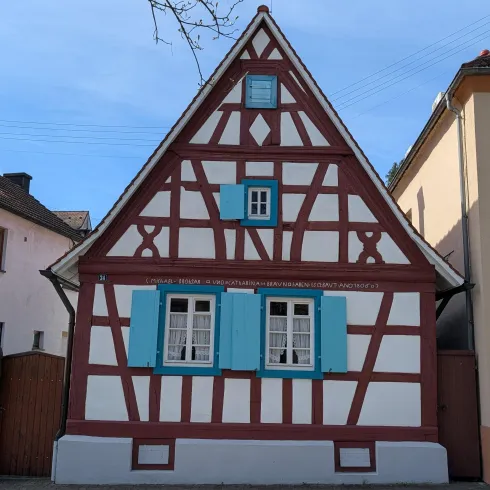 Ein charmantes Fachwerkhaus mit blauen Fensterläden. Der Himmel ist klar und es ist ein schöner Tag.
