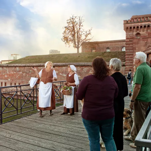  Eine Gruppe lauscht gespannt den Worten von zwei Bauersfrauen vor dem Weißenburger Tor