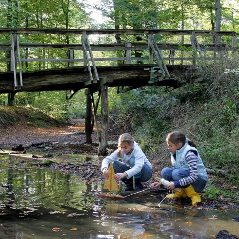 Zwei Mädchen spielen mit einem kleinen Segelboot an einem flachen Bach im Wald